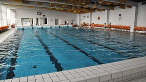 A large indoor swimming pool with multiple lanes, a lifeguard station, and seating areas with orange chairs. - Hotel Panon (Hodonin)