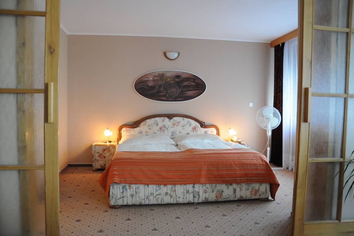 Una camera da letto con un letto, due lampade ai comodini, una ventola a parete e un quadro sopra il letto.