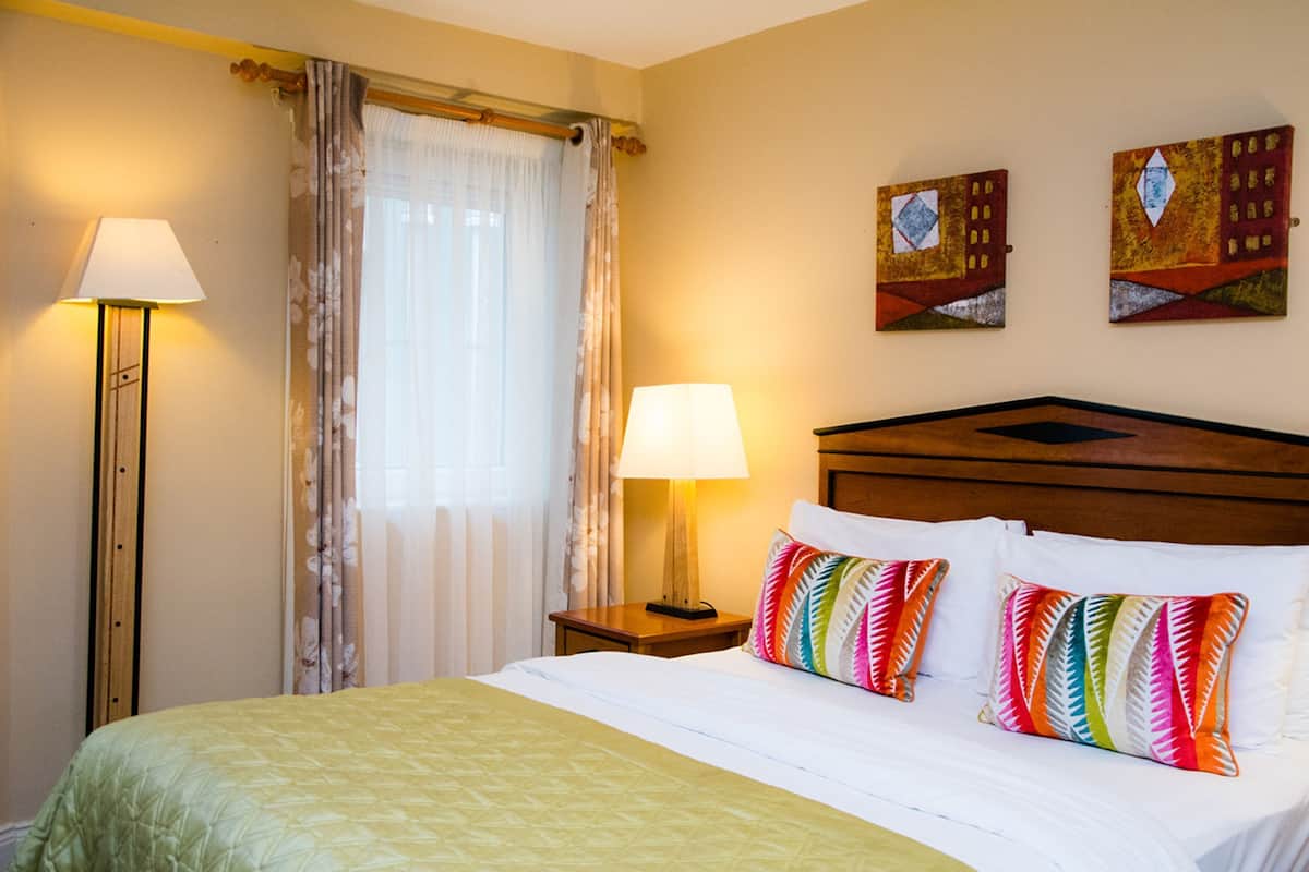 Une chambre d’hôtel comprenant un lit, deux lampes de chevet, une fenêtre avec des rideaux et deux œuvres d’art murales.