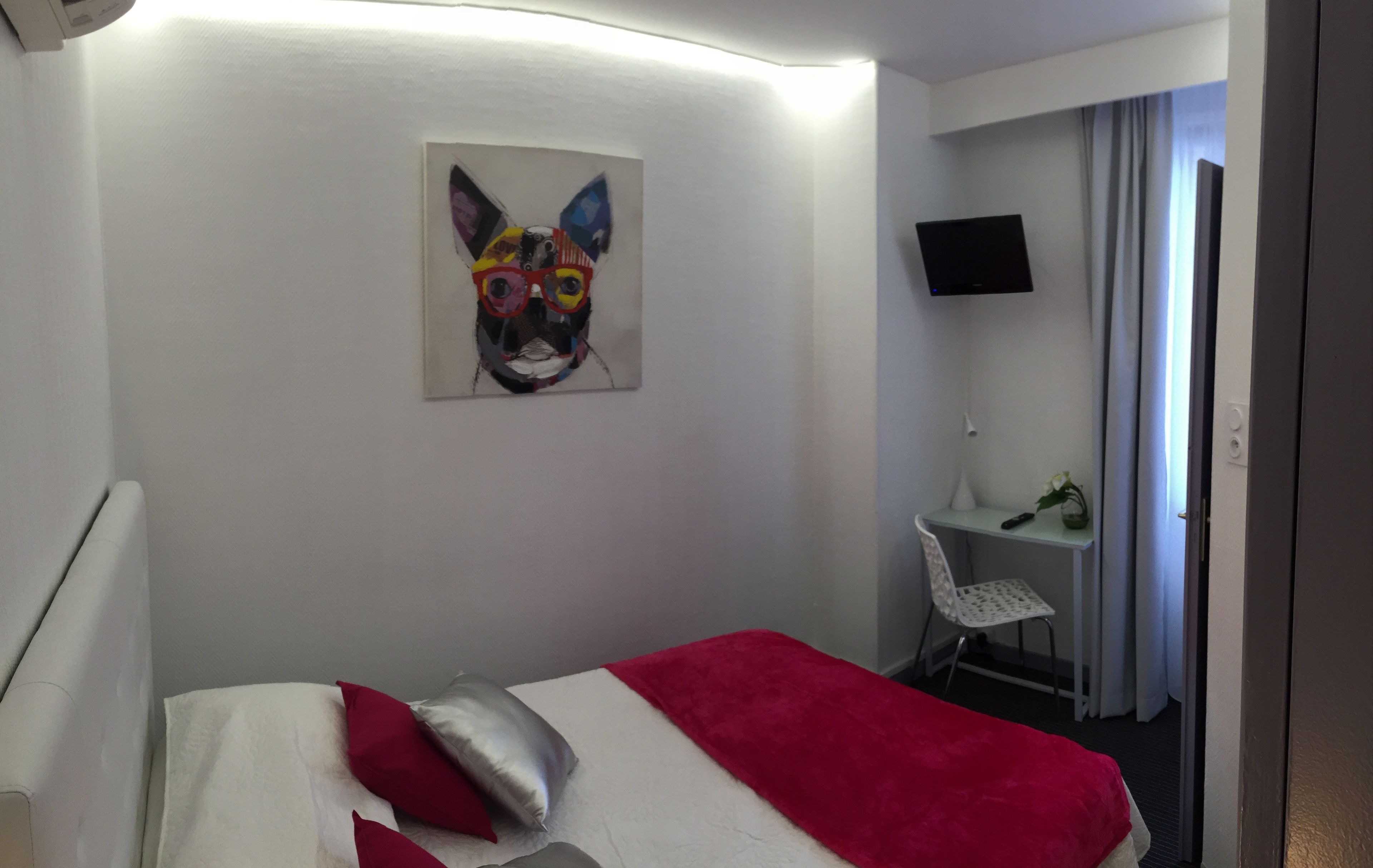 Una habitación de hotel con cama, escritorio, silla, televisor y un cuadro en la pared.
