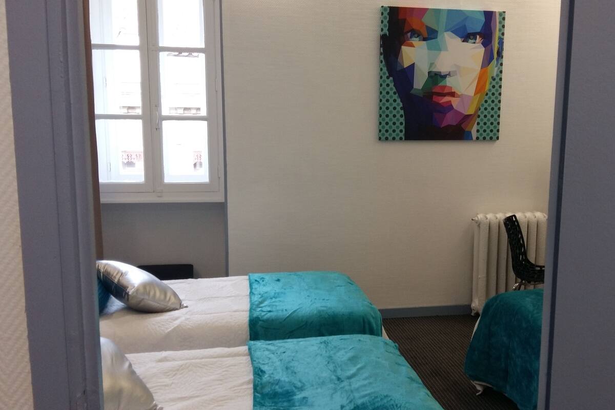 Ein Hotelzimmer mit zwei Betten, einem Fenster, einer Heizung und einem farbenfrohen Bild an der Wand.