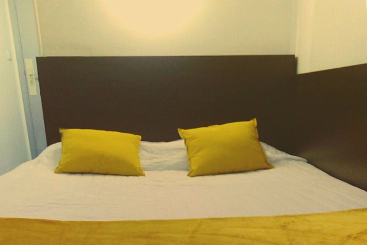 Ein Bett mit weißer Bettdecke, zwei gelben Kissen, einer braunen Decke und einem dunklen Kopfteil.