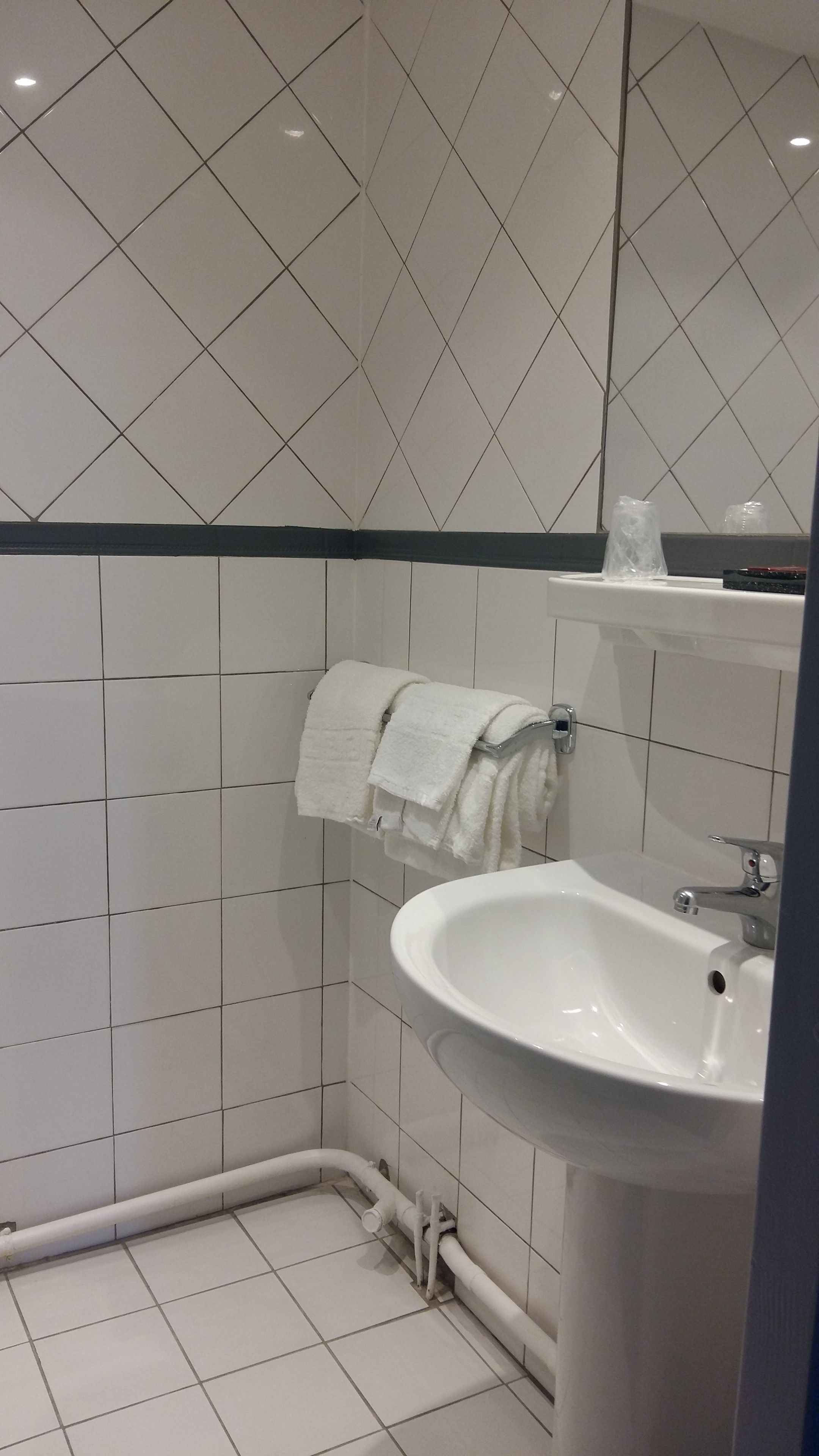 Une salle de bain avec des murs recouverts de carreaux blancs, un lavabo blanc et un porte-serviettes avec une serviette blanche.