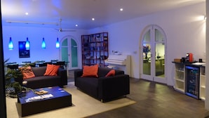 Een moderne woonkamer met twee zwarte banken, een salontafel, een boekenkast en een zichtbare keukenruimte via een rondboogvormige deuropening.