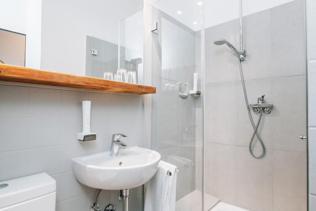 A modern bathroom with a glass shower enclosure, a white sink, and a wooden shelf above the sink.
