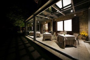 An outdoor dining area with tables and chairs, large windows, and a stone wall. - Tenuta Ponziani - Griffin's Resort (Orvieto)