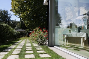 A garden pathway leading to a building with a glass facade, a table with a tablecloth, and red flowers. - Tenuta Ponziani - Griffin's Resort (Orvieto)