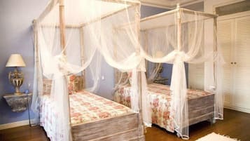 Una cama con dosel y cortinas florales en una habitación con suelo de madera y pared azul.