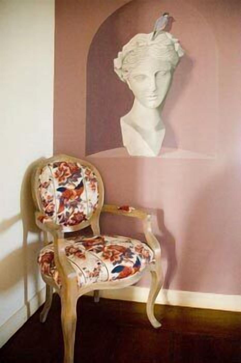 A chair with floral upholstery and a bust sculpture on the wall behind it.