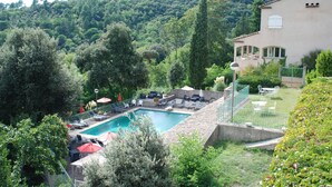 Una piscina con lettini e ombrelloni, circondata da vegetazione e da una collina.