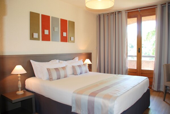 A hotel room with a large bed, two bedside lamps, a headboard, and a view of the outdoors through a sliding door. - Hôtel 3* La Vallée des 3 Barbus  (Generargues)