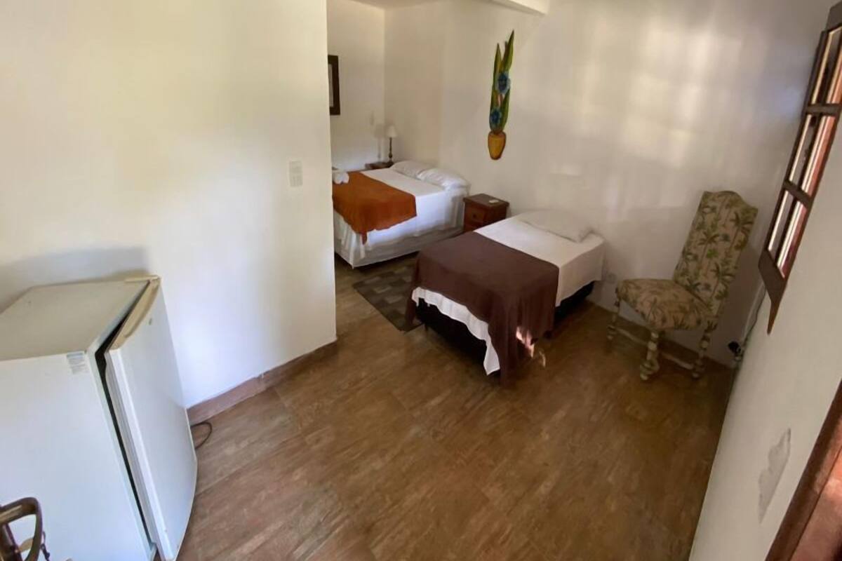 A compact hotel room with a bed, a chair, a small table, and a refrigerator.