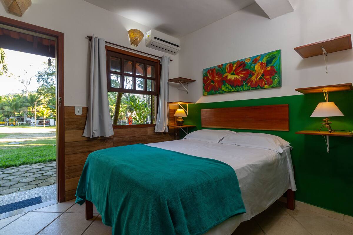 A hotel room with a bed, a window with curtains, a painting on the wall, and a lamp on a bedside table.