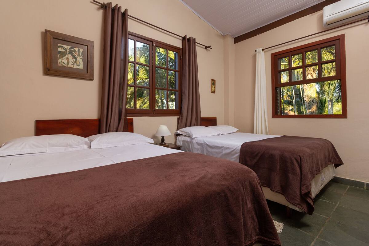 A hotel room with two beds, a window with curtains, a wall-mounted air conditioner, and a framed picture.