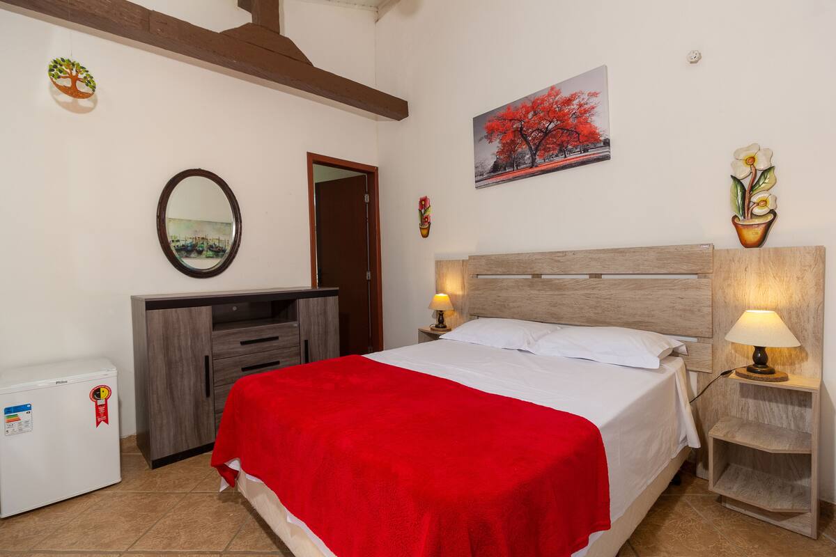 A hotel room with a bed, a desk, a chair, a lamp, and a small refrigerator.