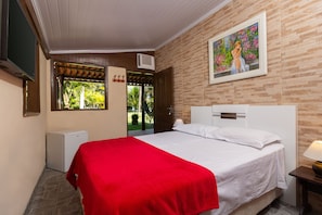 Quarto de hotel com cama, televisão, pequeno frigorífico e um quadro na parede.