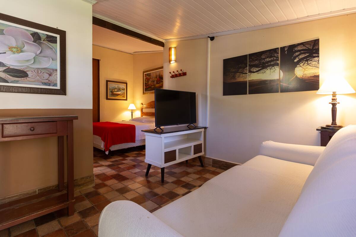 A hotel room with a bed, a TV on a white stand, a desk, and artwork on the walls.