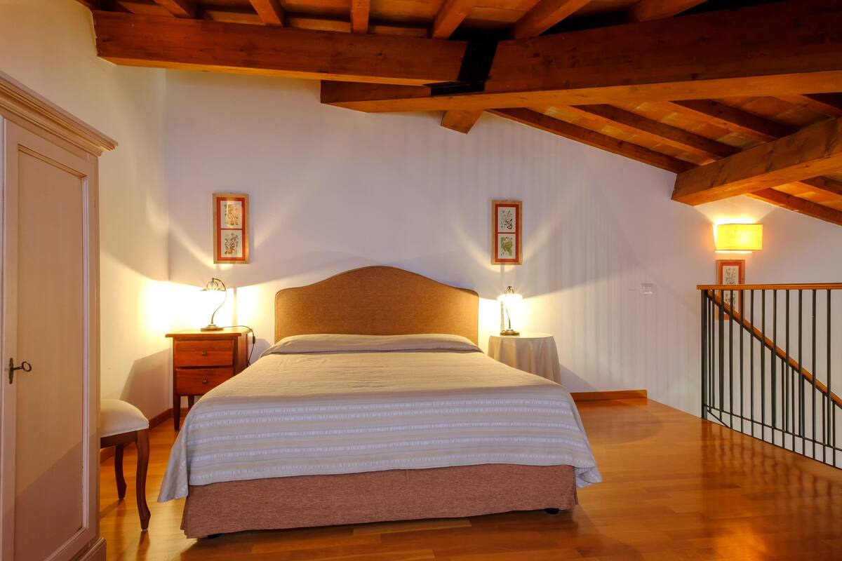 Une chambre avec un plafond en bois, un grand lit, deux tables de chevet avec des lampes et un escalier.