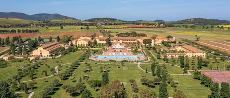 An aerial view of a large estate with multiple buildings, a central swimming pool, and extensive green lawns.