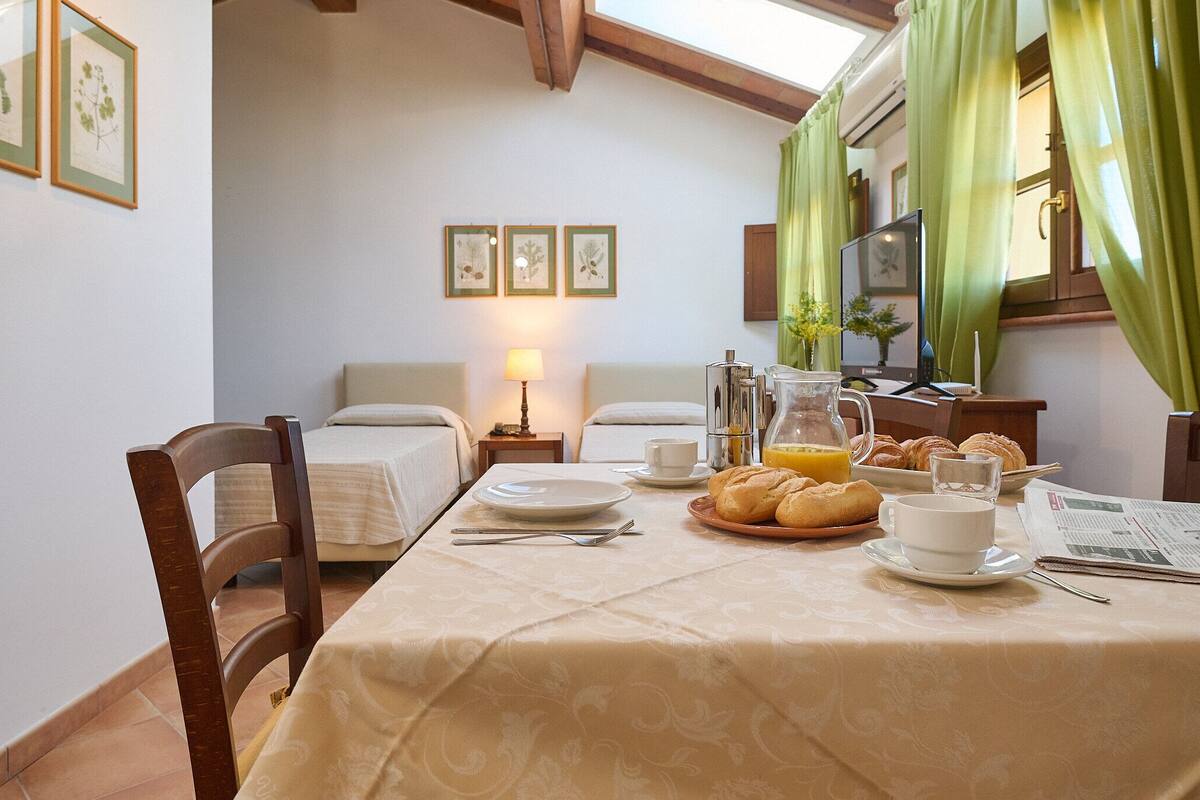 Une table, des chaises et un lit sont disposés dans une pièce pour le petit-déjeuner. La pièce est dotée d’un plafond en bois et de rideaux verts.
