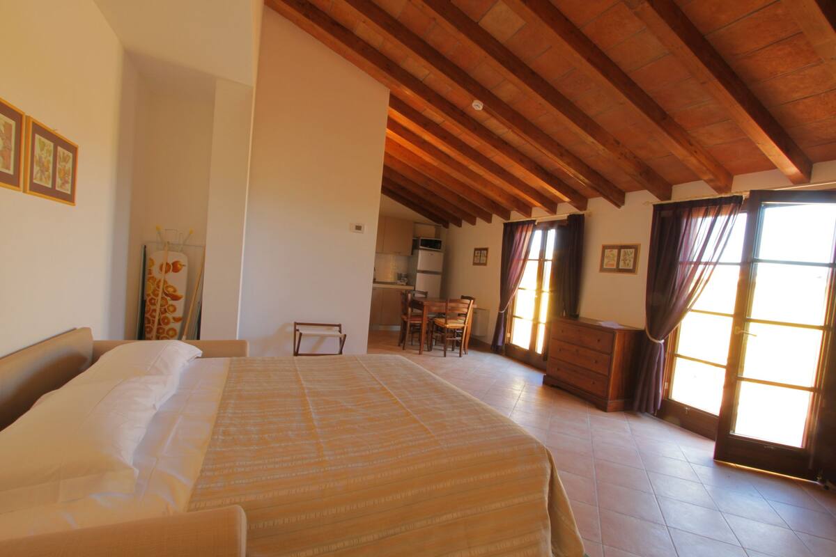 Une chambre spacieuse avec un grand lit, un plafond en bois et une vue sur la cuisine et la salle à manger.