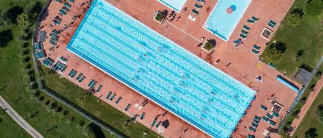 Vista aérea de un complejo de piscinas con múltiples carriles, tumbonas y una zona de piscina separada.