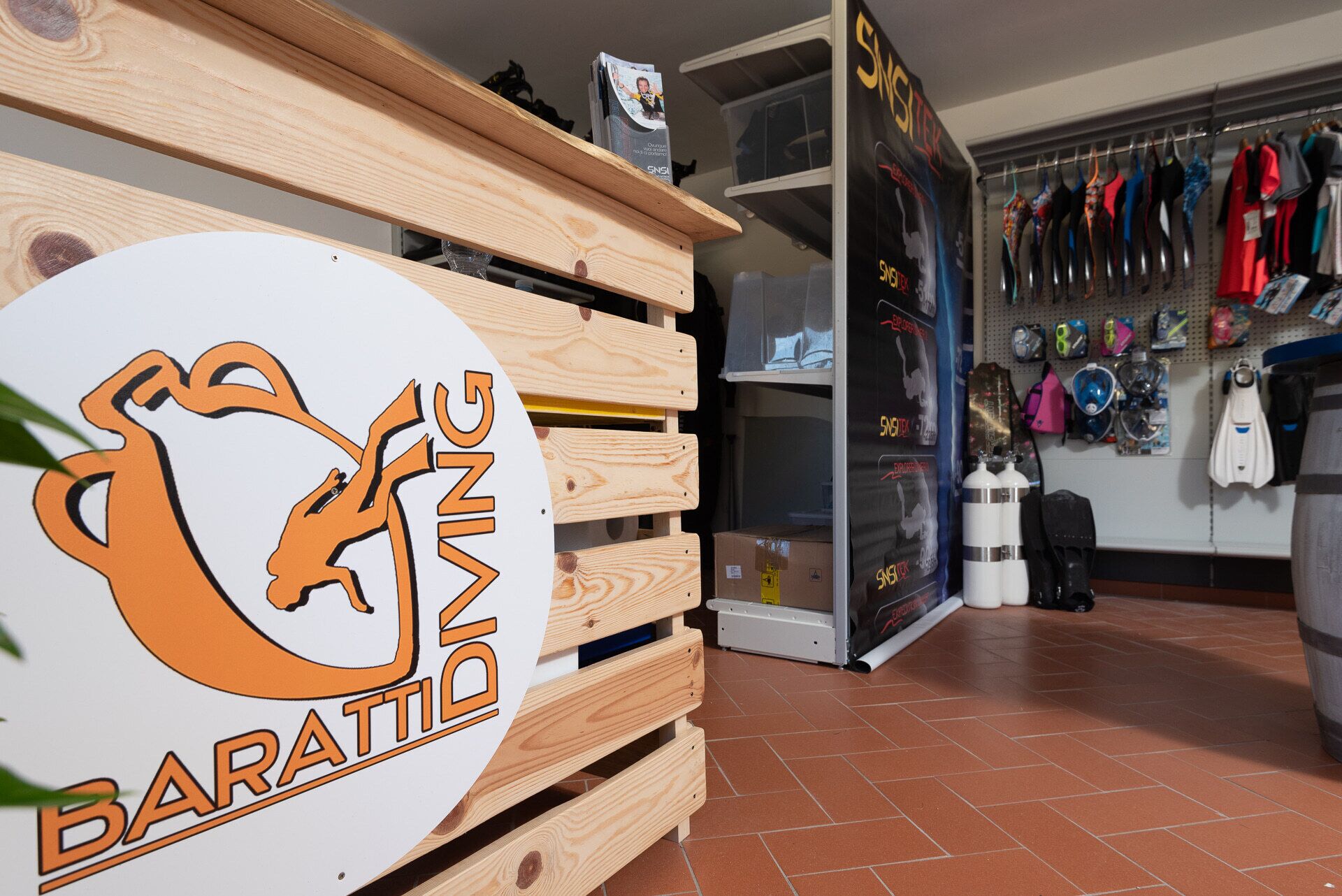 A wooden counter with a logo, shelves with items, and a wall displaying diving gear.