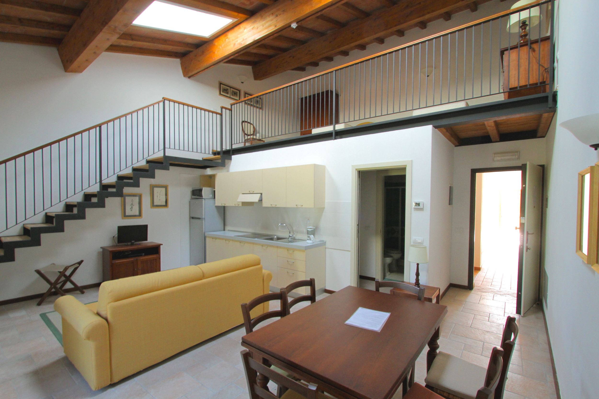 Un vaste espace de vie comprenant un canapé jaune, une table à manger en bois et un escalier menant à un niveau supérieur.