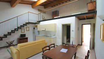 A spacious living area with a yellow sofa, wooden dining table, and a staircase leading to an upper level.