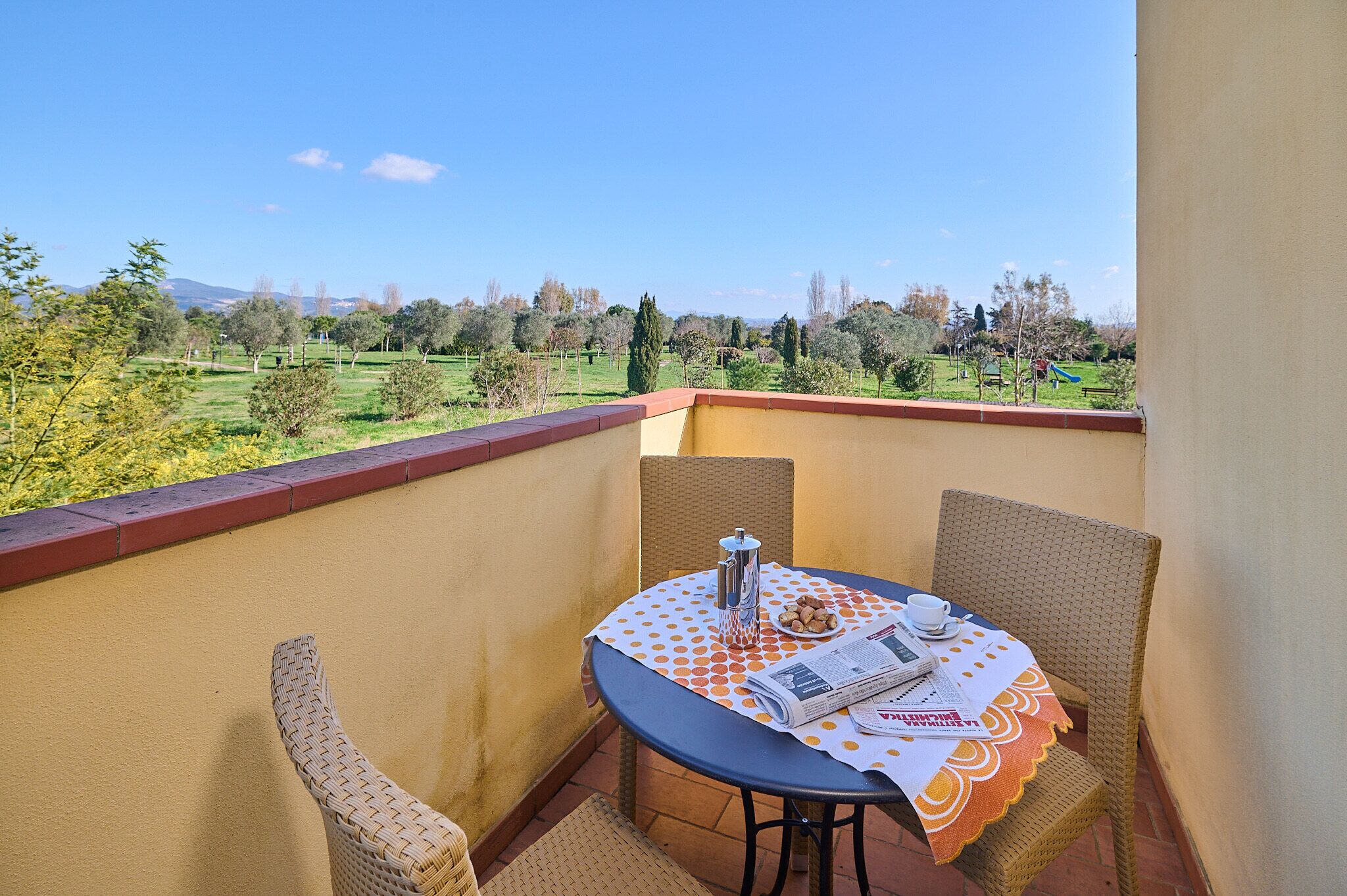 A balcony with wicker chairs, a table with a newspaper, a cup, and a pitcher.