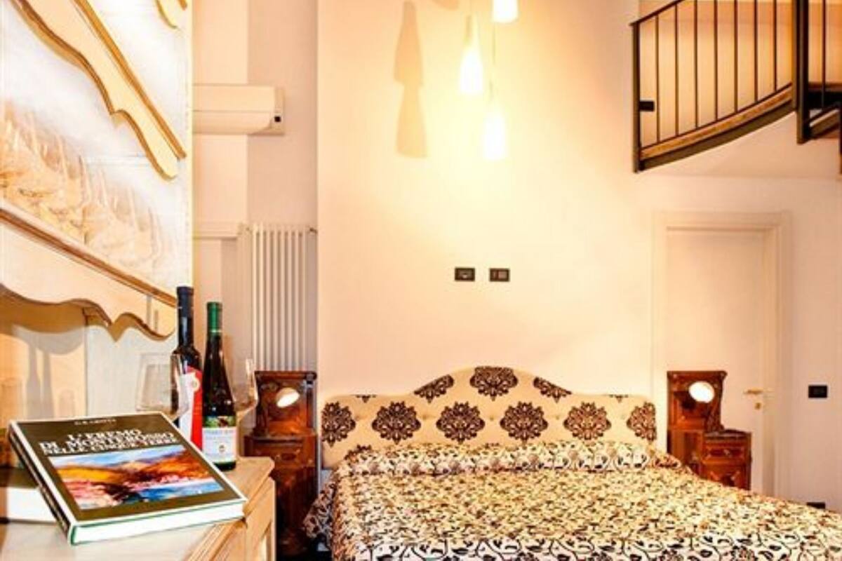 Un dormitorio con cama, mesita de noche, un libro, una botella y un radiador fijado a la pared.