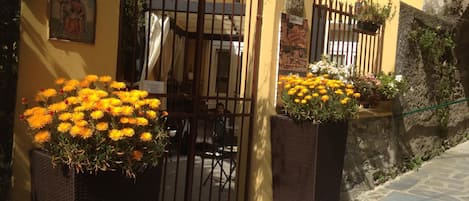 A yellow building with a gated entrance, potted yellow flowers, and a stone wall.