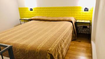 Una cama individual con una colcha estampada en una habitación con pared de ladrillo amarillo y una pequeña mesa con una silla.