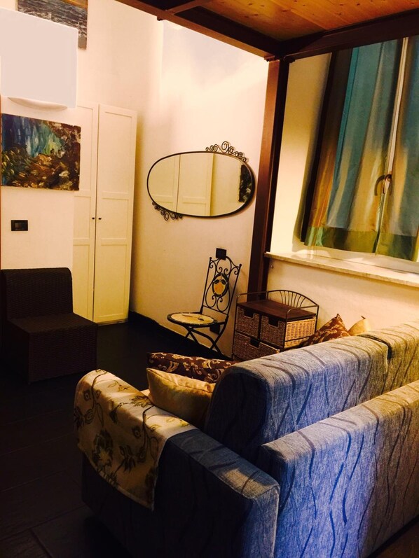 Una sala de estar acogedora con un sofá, una silla, una mesita, un espejo y una ventana con cortinas.