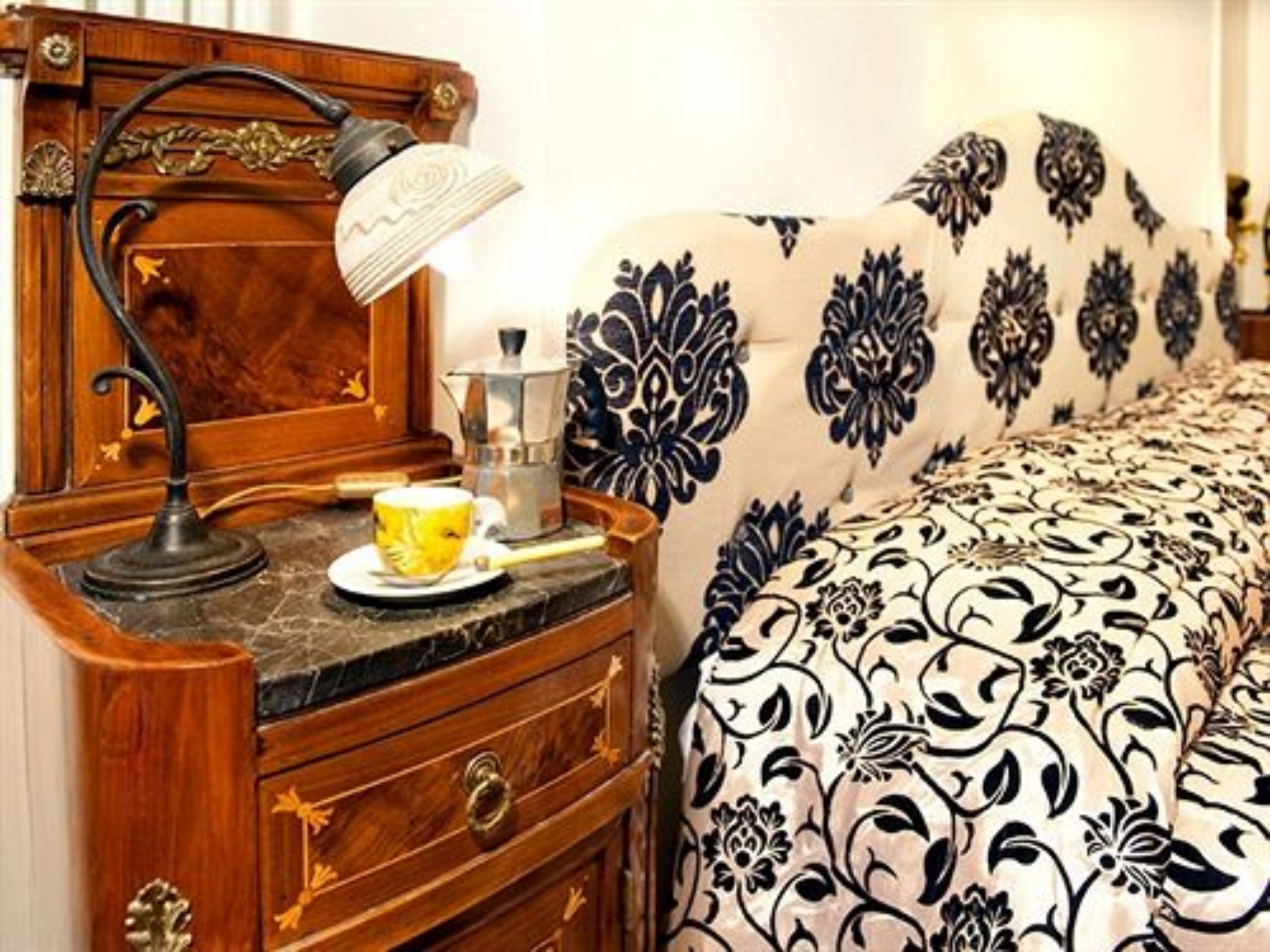 Un comodino in legno con una lampada, una tazza e una caffettiera.
