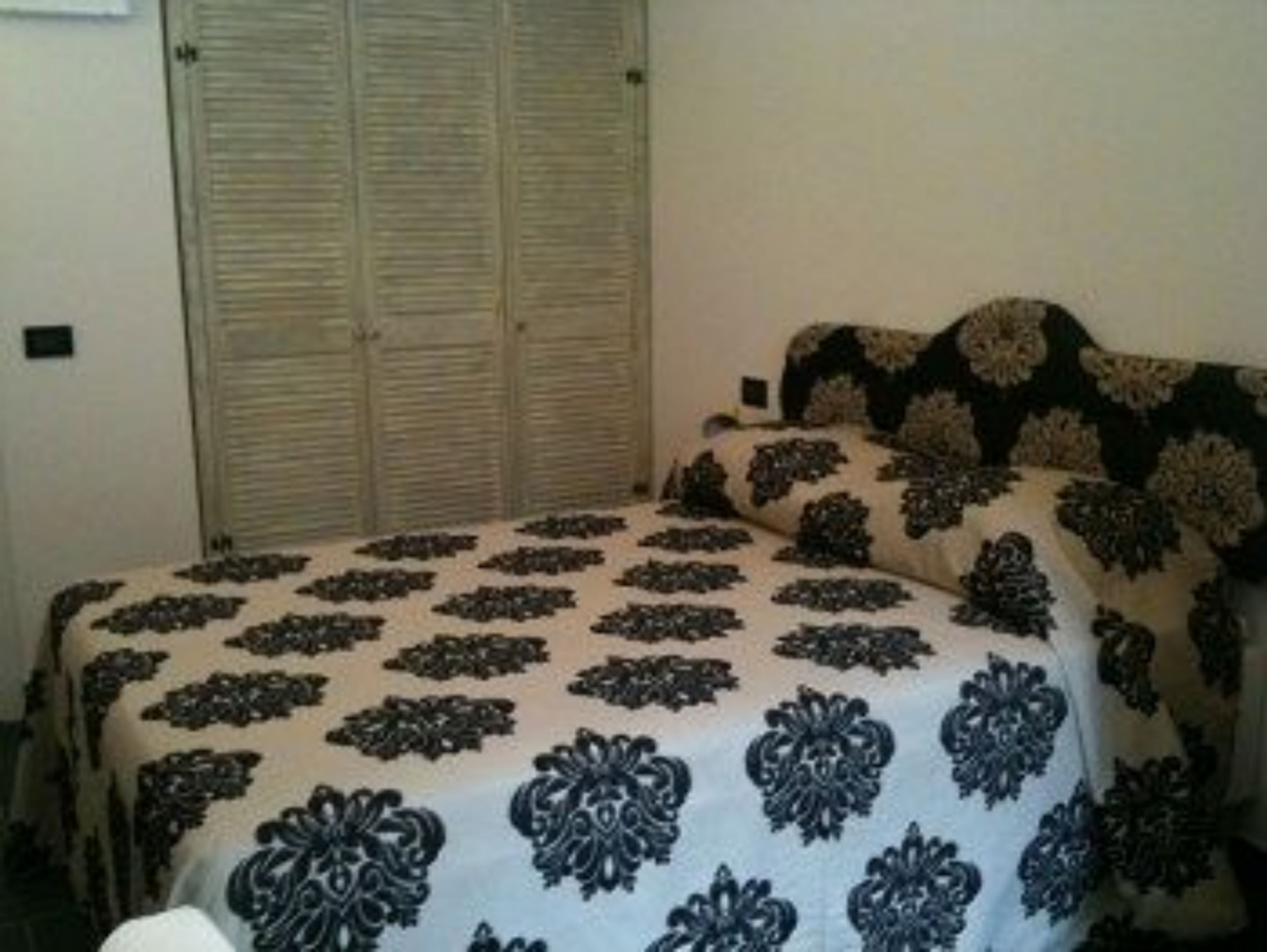 Une chambre à coucher avec un lit recouvert d’une couvre-lit à motifs, une armoire fermée et un mur uni.