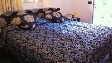 A bed with a patterned bedspread and matching pillows, a nightstand with a lamp, and a window with curtains.