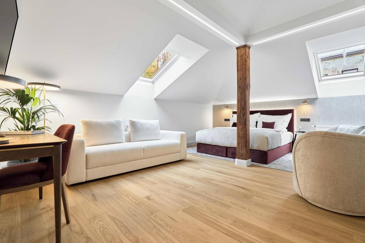 A modern loft bedroom with a skylight, a sofa, a bed, and a dining area.