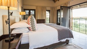 A bedroom with a large bed, a nightstand with a lamp, and a view of the outdoors.