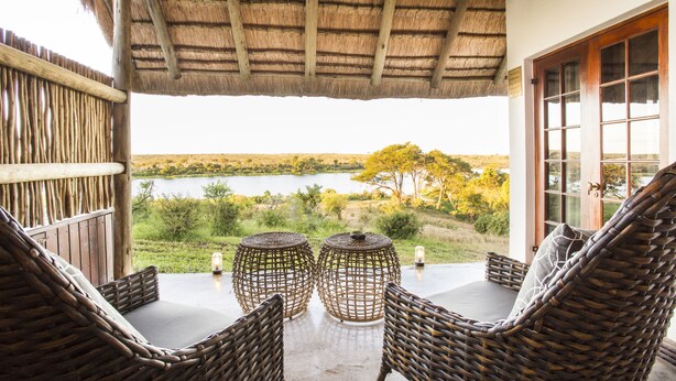 A thatched-roof veranda with wicker furniture and a view of a lake.