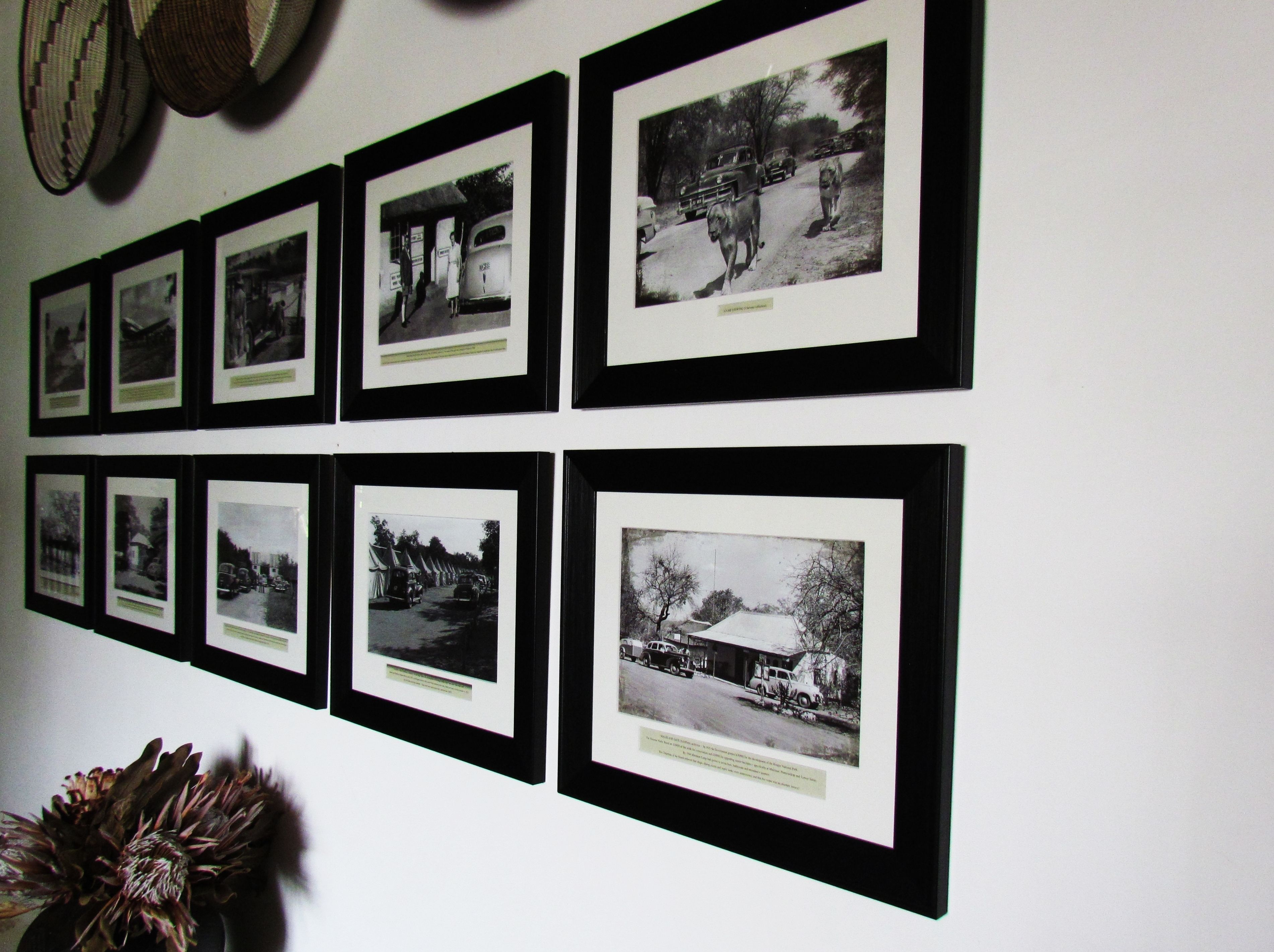A wall with multiple black and white photographs in frames, depicting various scenes including vehicles and buildings.