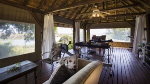 A wooden deck with a thatched roof, a sofa, and a dining table with chairs.