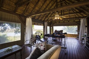 Una terraza de madera con techo de paja, un sofá y una mesa de comedor con sillas.