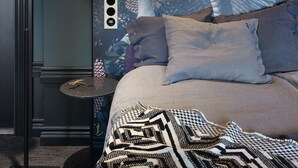 Un dormitorio con una cama grande, un mural en la pared, una lámpara moderna y una mesita redonda.