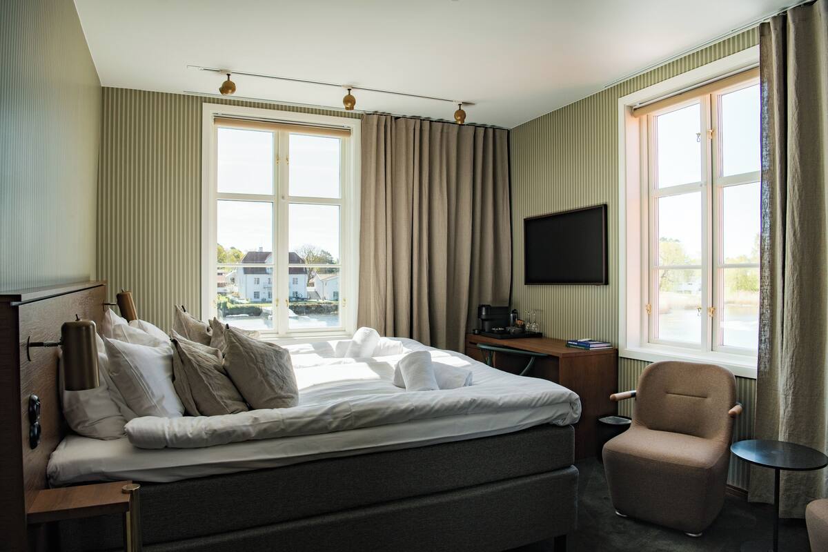 A hotel room with a large bed, a desk, a chair, and a TV mounted on the wall.