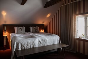 A bedroom with a bed, bedside lamps, a window with curtains, and a wooden bench.