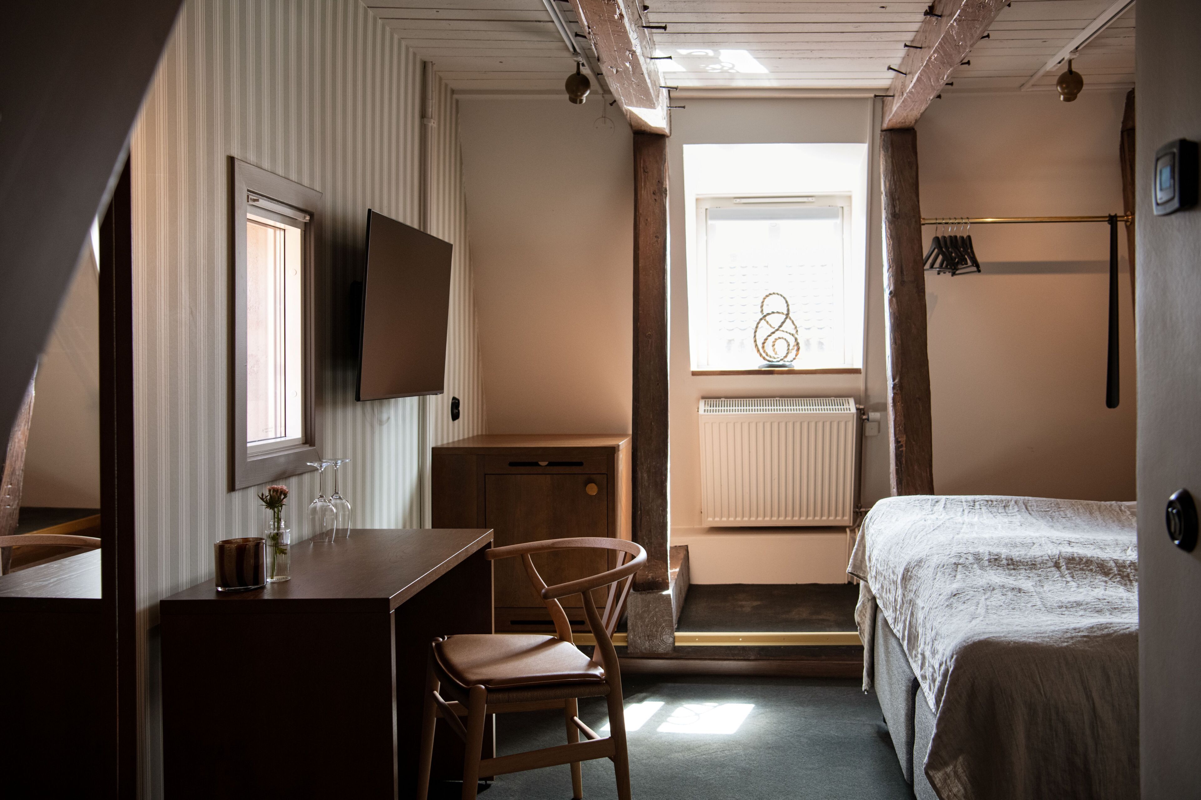 Un dormitorio con cama, escritorio, silla, televisor y ventana con radiador.