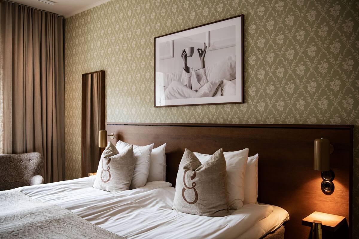 A neatly made bed with a headboard, a framed picture on the wall, and a bedside lamp.