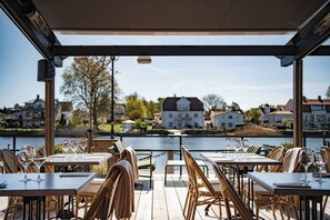 An outdoor dining area with tables and chairs, overlooking a body of water and residential buildings.