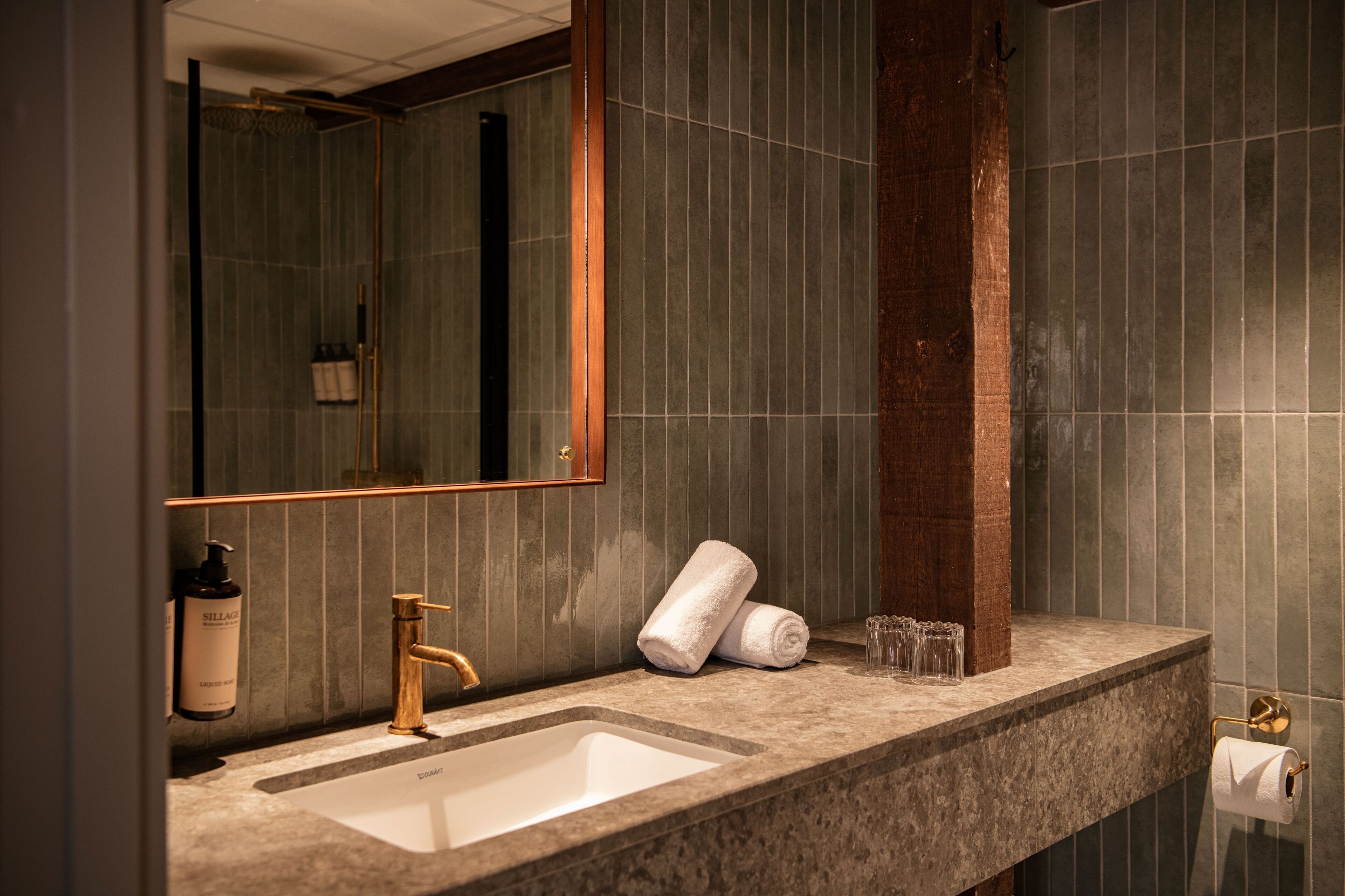 Un baño con lavamanos, espejo, toalla y artículos de aseo.